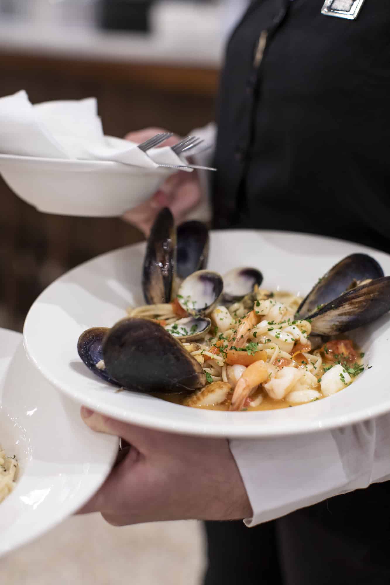 Photo of waiter holding a plate of seafood pasta with mussels