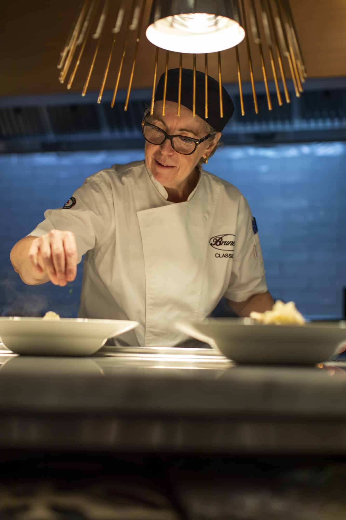 Photo of a Brunetti Classico Chef under a kitchen heat light sprinkling ingredients into a plate