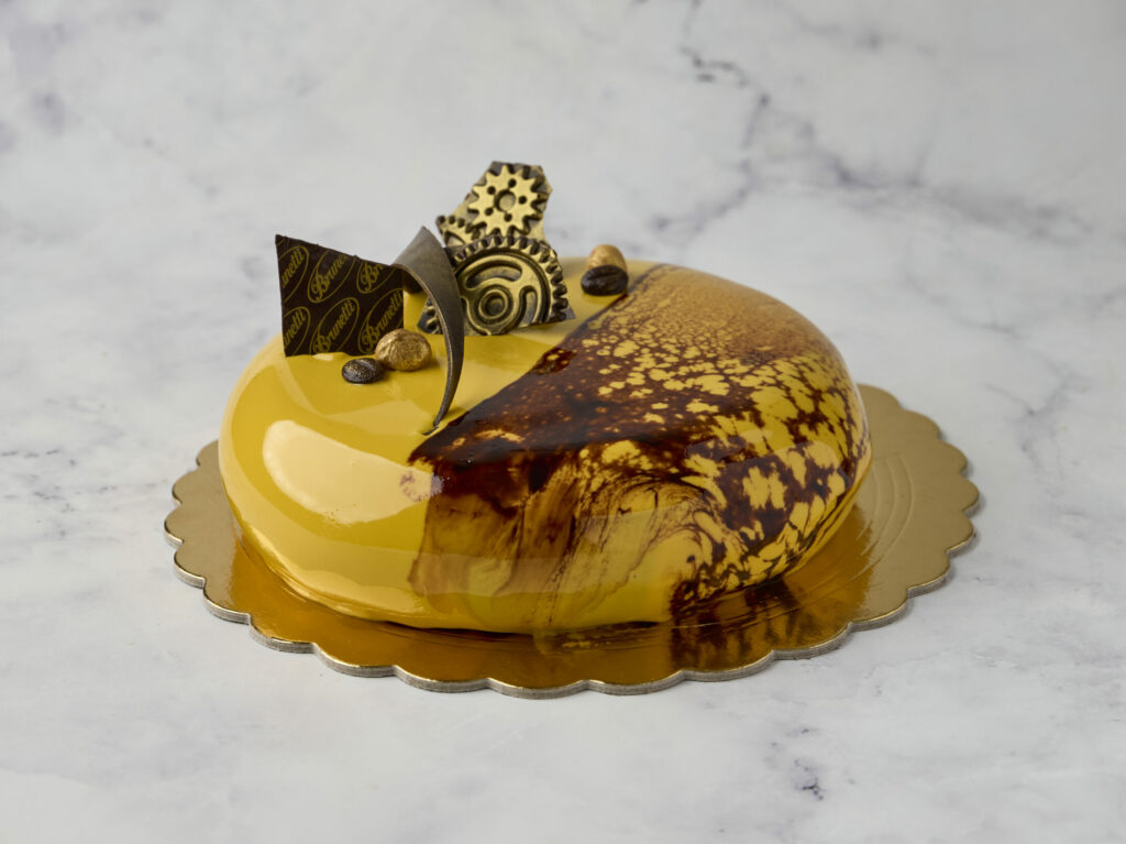 Celebrate Father’s Day with Brunetti Classico's cake: hazelnut mousse, coffee crèmeux, and salted caramel on banana sponge, glazed in vivid yellow with chocolate decor.